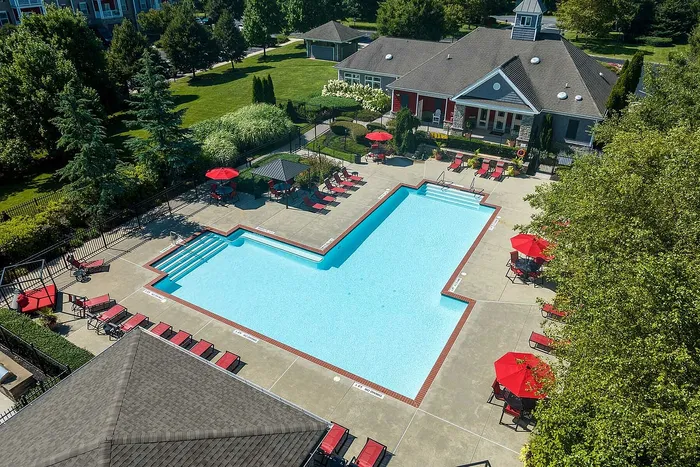 Aerial view of a luxurious outdoor pool with red umbrellas and sun loungers surrounded by lush greenery.