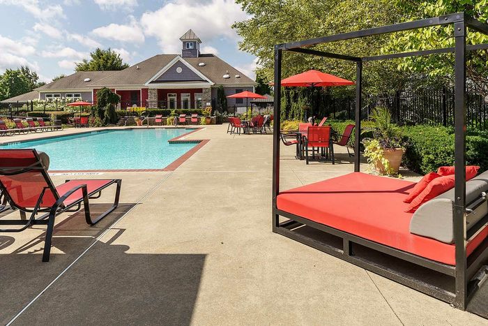 Inviting outdoor pool area with modern sun loungers, red umbrellas, and lush greenery.