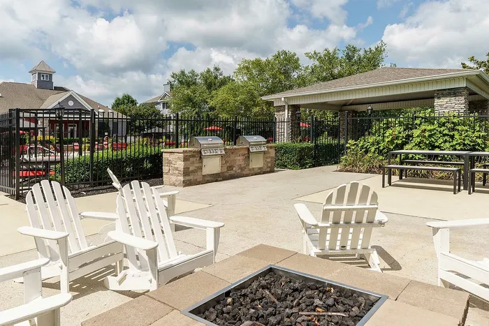 Inviting outdoor area with white Adirondack chairs, a fire pit, barbecue grills, and a scenic garden view.