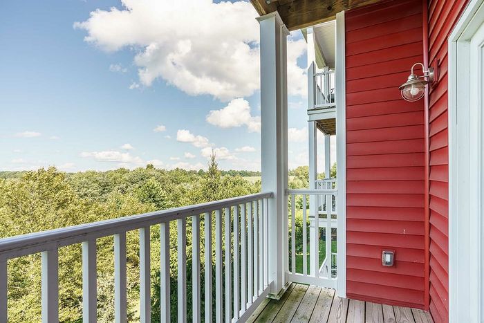 Inviting balcony with red exterior, offering a serene view of lush greenery and a bright sky.