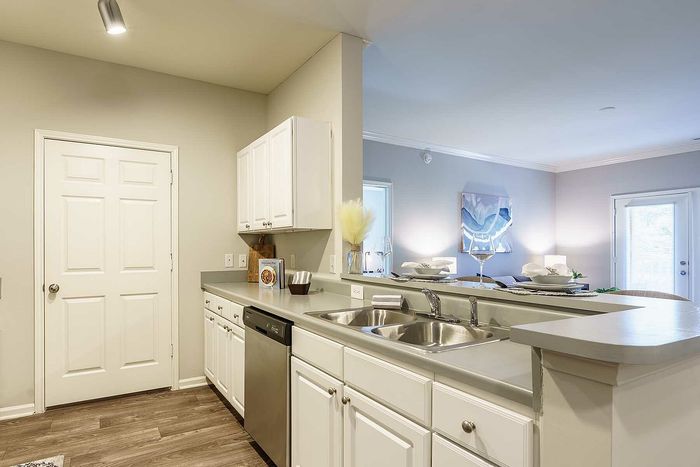 Bright kitchen with white cabinets and stainless steel appliances leading into a modern living room.