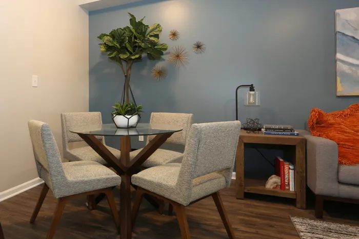 Modern dining area with elegant chairs around a glass-top table, lush green plant, and stylish wall decor.