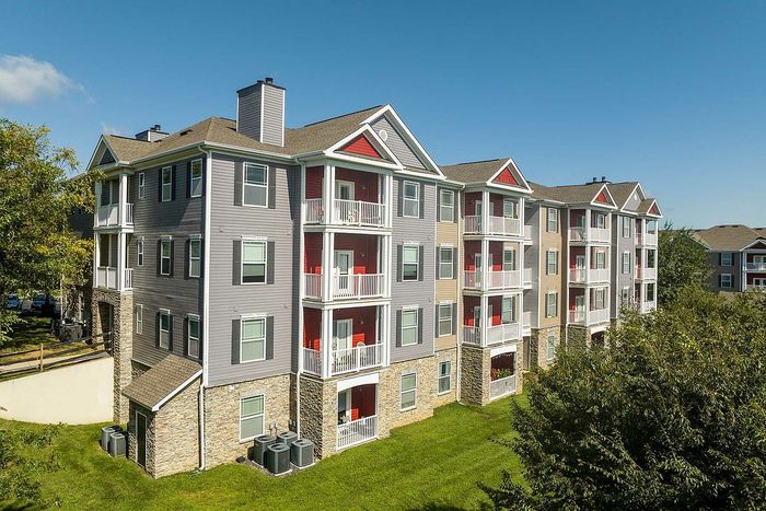 Charming four-story apartment building with balconies, nestled in a lush green setting on a sunny day.