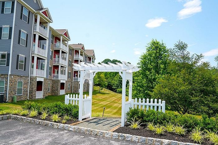 Elegant apartment complex with balconies, white fencing, and lush greenery.