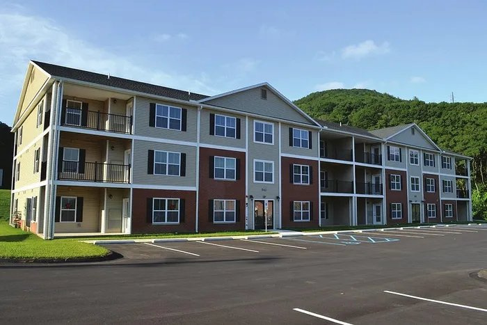 Charming three-story apartment complex with spacious balconies, surrounded by lush greenery and ample parking space.