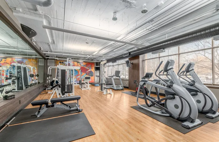 Modern fitness center with state-of-the-art equipment, colorful mural, and ample natural light.