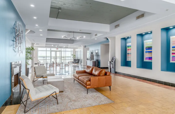 Elegant apartment lobby with modern decor, featuring a cozy seating area with a leather sofa, vibrant artwork, and expansive windows offering Lake Erie views