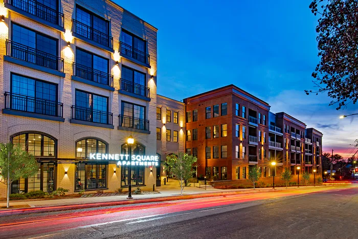 Elegant Kennett Square Apartments exterior at dusk, showcasing modern architecture with warm lighting and large windows.