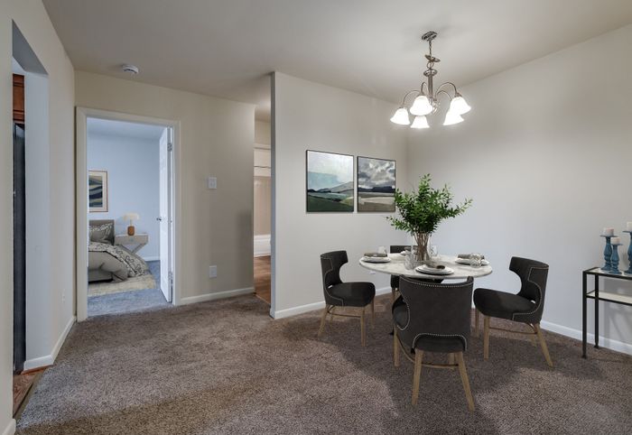 Inviting dining area with elegant chandelier lighting, featuring modern decor and a cozy, furnished bedroom in the background.