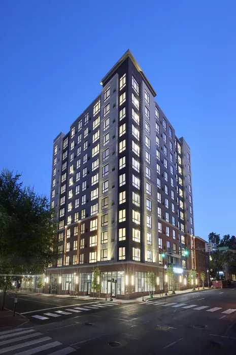 Contemporary high-rise apartment building illuminated against a twilight sky, showcasing a sleek urban design and large windows.