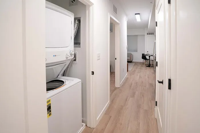 Modern apartment hallway with wood flooring, featuring an in-unit washer and dryer and leading to a cozy dining area.
