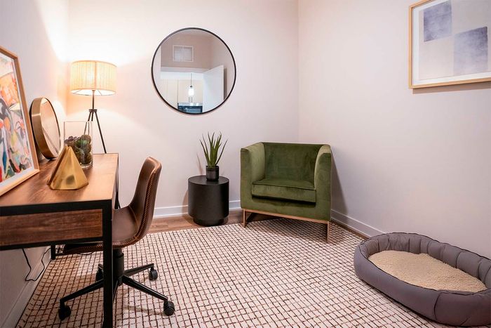 Cozy home office with stylish decor featuring a wooden desk, chic lamp, modern art, and a plush green armchair.