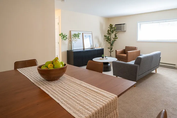 Inviting living space with stylish grey and brown seating, modern table setup with fresh fruit centerpiece, and lush green plant accents.