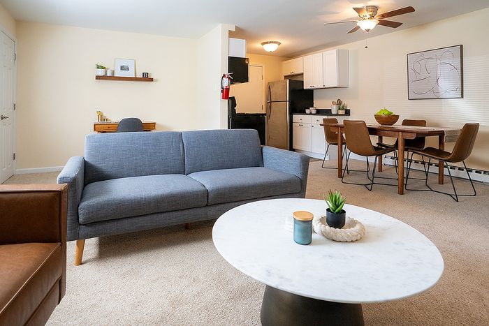 Modern open-concept living area with a stylish blue sofa, a chic marble coffee table, and an elegant dining set by a cozy kitchen.