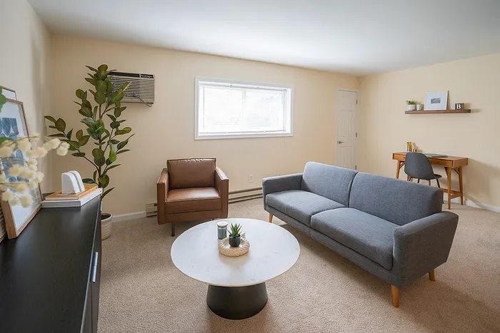 Bright and inviting living room with modern furniture, lush indoor plant, and a cozy workspace corner.