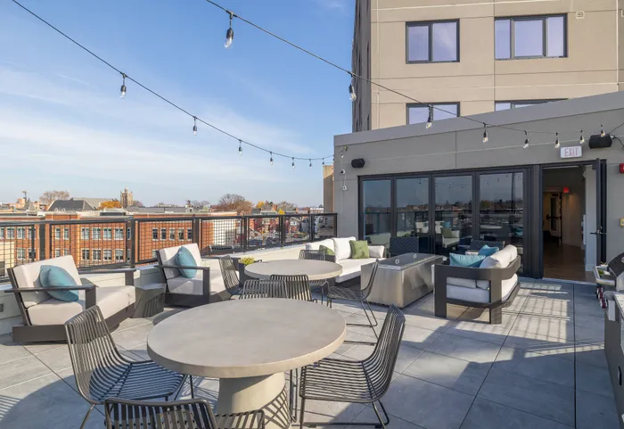 Sophisticated rooftop terrace with ample seating, contemporary decor, and panoramic city views under twinkling string lights.