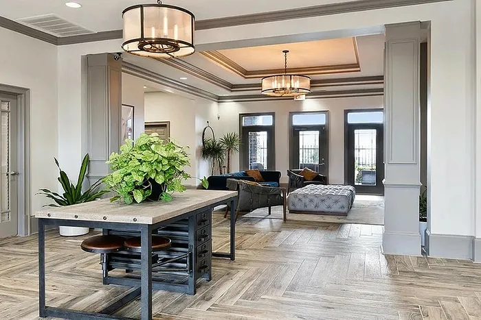 Elegant open-concept living space with stylish lighting, chic wooden flooring, and vibrant greenery, leading to a cozy seating area with abundant natural light.