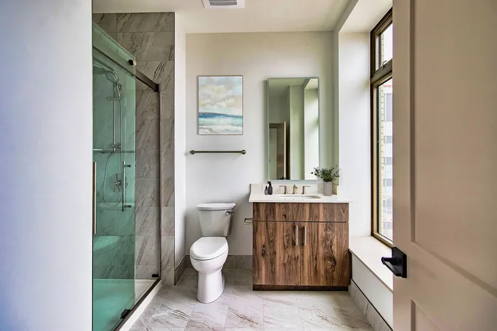 Sleek bathroom with glass-enclosed shower, modern vanity, and large window for natural light.