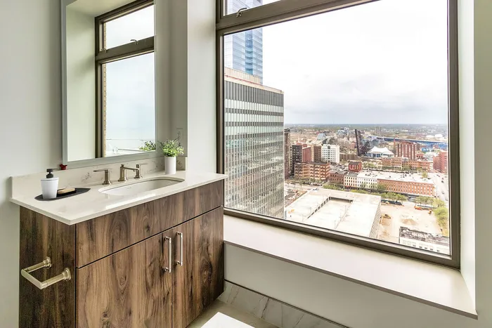 Luxurious bathroom with modern wooden vanity and expansive cityscape view from large window.