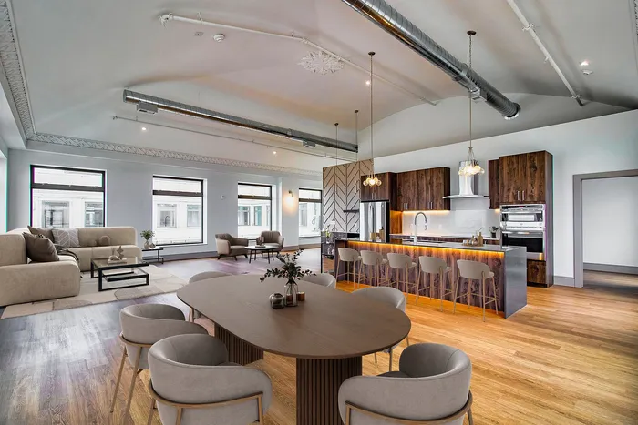 Luxurious open-plan loft with high ceilings, featuring a modern kitchen island, stylish wooden accents, and expansive windows for natural light.