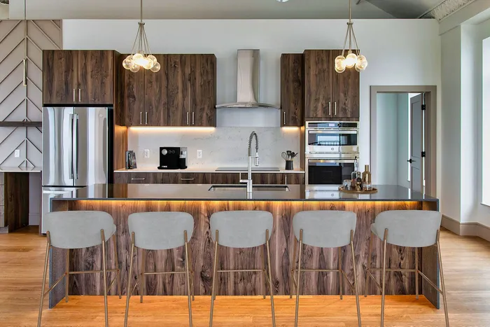 Contemporary kitchen with sleek wooden cabinetry, a central island with bar stools, and modern appliances under chic pendant lights.