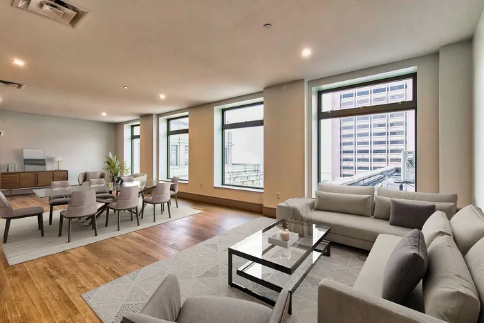 Inviting modern living space with large windows, elegant wooden flooring, and stylish furniture, ideal for urban living.