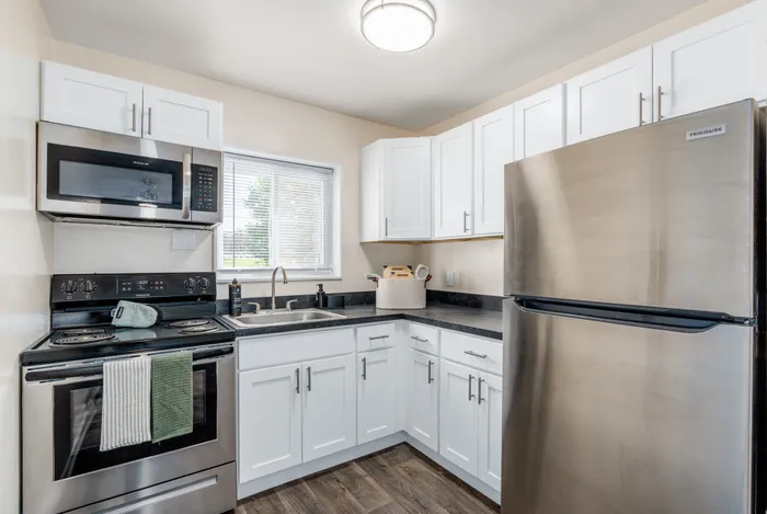 Modern kitchen with sleek stainless steel appliances, bright white cabinetry, and a cozy window offering natural light.