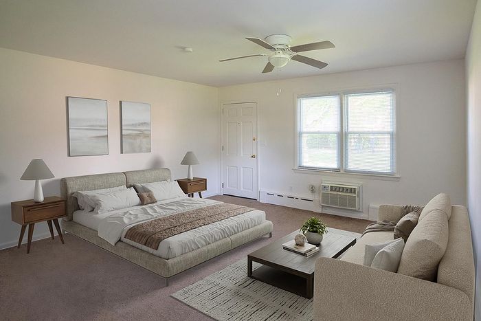 Spacious sunlit bedroom with elegant decor, featuring a cozy bed, stylish sofa, and chic coffee table, complemented by modern nightstands and serene artwork.