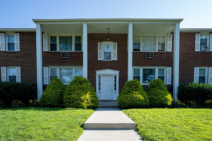 Inviting red brick apartment building with lush greenery and charming white shutters, exuding classic elegance and comfort.