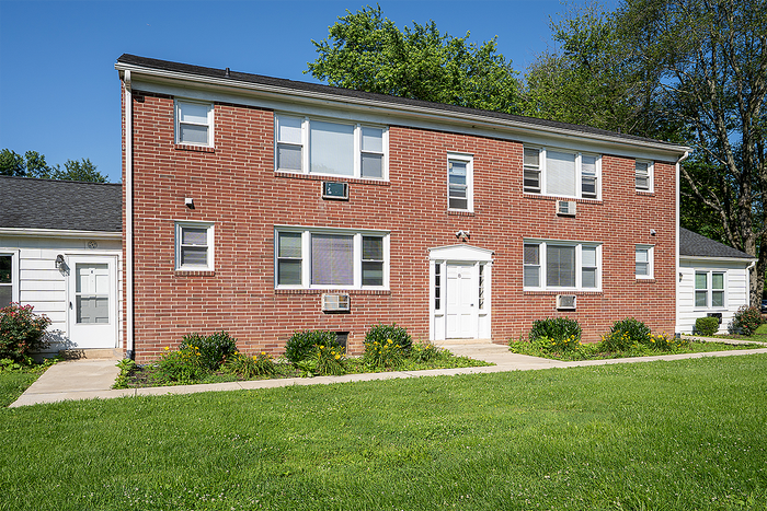 Charming brick apartment building with lush green surroundings, featuring ample windows for natural light.
