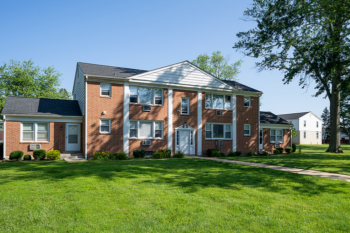 Charming red brick apartment building surrounded by lush green lawn and mature trees, offering a serene and inviting ambiance.