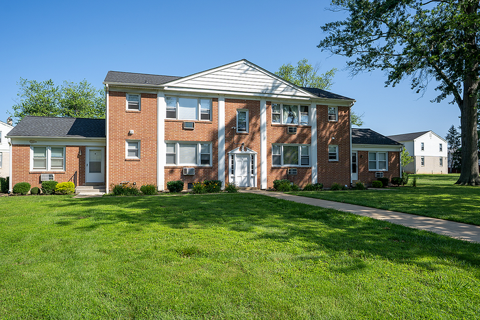 Charming brick apartment building with lush green lawn, offering serene suburban living.