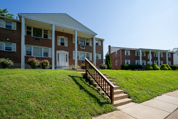 Charming brick apartment building with classic architecture, surrounded by lush greenery and a welcoming entrance.