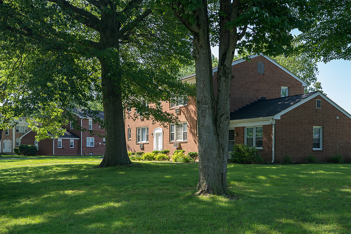 Charming brick apartment complex surrounded by lush green lawns and mature trees, perfect for serene living.