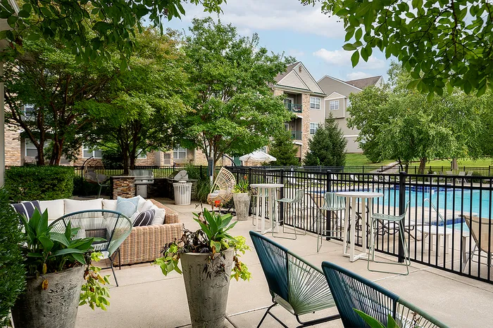 Chic outdoor patio area with lush greenery, modern lounge furniture, and poolside views at a luxurious apartment complex.