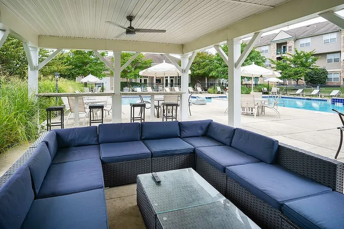 Chic outdoor lounge area with cozy seating under a stylish pergola, overlooking a sparkling pool with lush greenery and modern amenities.