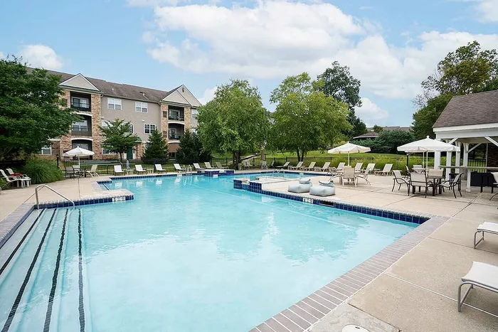 Charming apartment complex featuring a sparkling pool with lounge chairs, surrounded by lush greenery and a relaxed outdoor seating area under umbrellas.