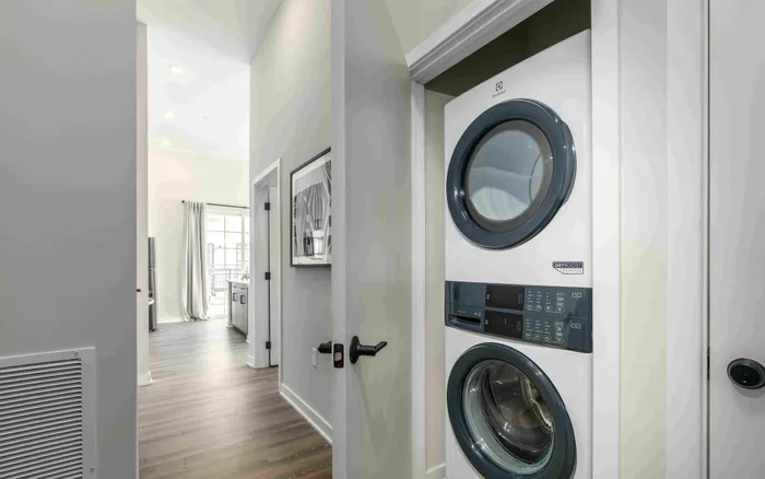 Modern apartment hallway showcasing a sleek in-unit washer and dryer with a glimpse of the bright, airy living space and stylish wood flooring.