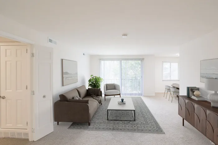 Bright and inviting living room with modern furniture, featuring a cozy brown sofa, artistic decor, and abundant natural light from large windows.