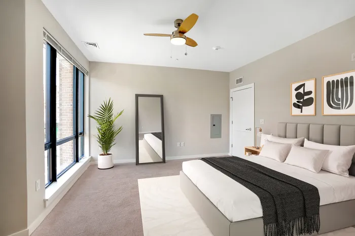 Bright and modern bedroom with large windows, sleek ceiling fan, and minimalist decor, offering a serene and inviting atmosphere.