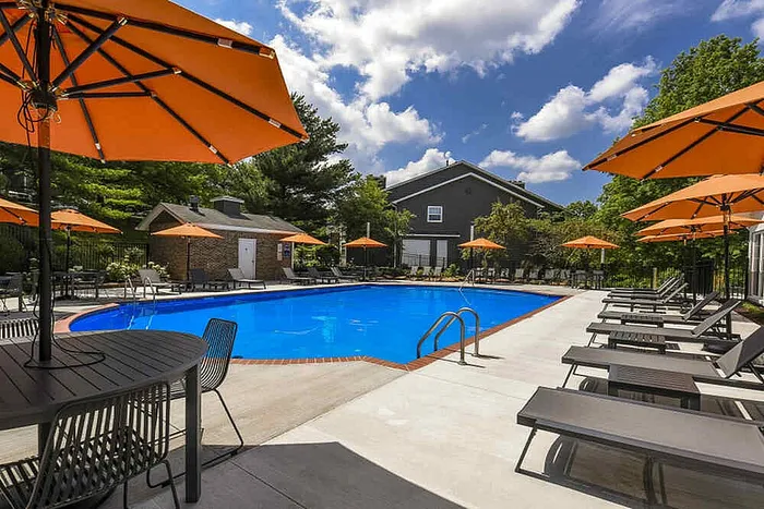 Inviting outdoor pool area with vibrant orange umbrellas, surrounded by lush greenery and comfortable lounge chairs, perfect for relaxation.