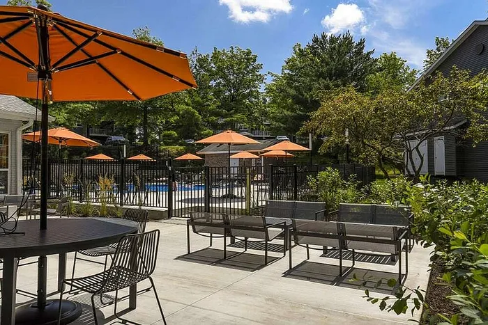 Chic outdoor seating area with vibrant orange umbrellas overlooking a sparkling pool, surrounded by lush greenery for ultimate relaxation.