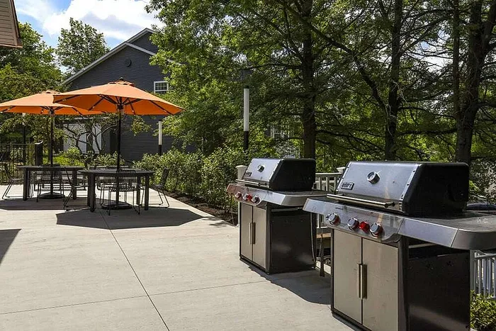 Inviting outdoor patio with modern barbecue grills and vibrant orange umbrellas, perfect for social gatherings in a lush green setting.
