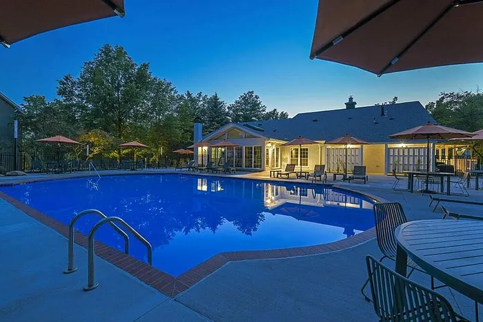 Luxurious apartment complex with a beautifully illuminated swimming pool area, surrounded by stylish seating and lush greenery, perfect for evening relaxation.