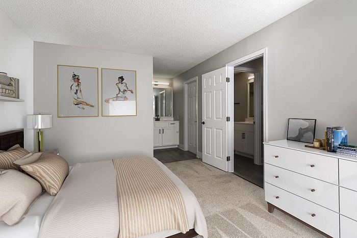 Inviting bedroom with elegant decor, featuring a comfortable beige bed, modern dresser, and access to a sleek private bathroom.