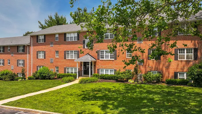 Charming three-story brick apartment building with lush greenery and inviting walkway on a sunny day.