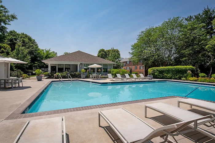 Inviting outdoor pool area with sun loungers and a modern clubhouse, set in lush greenery for a perfect summer retreat.