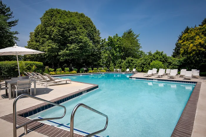 Luxurious outdoor pool area surrounded by lush greenery, featuring elegant lounge chairs and shaded seating, perfect for relaxation.