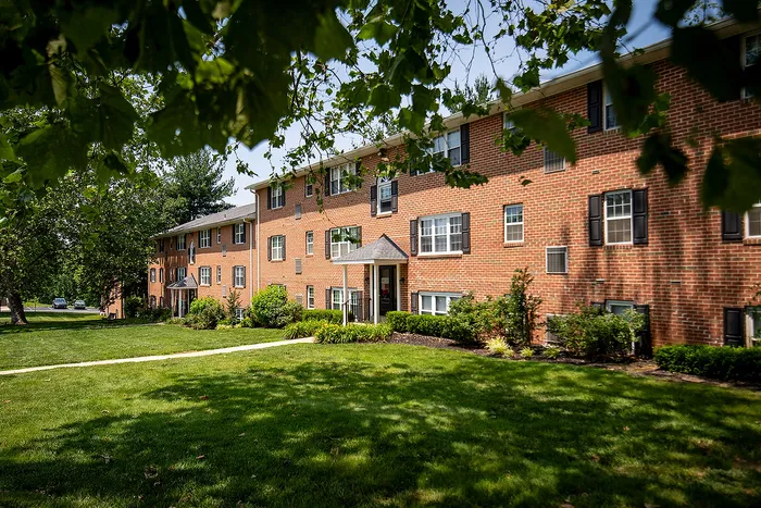 Charming brick apartment building surrounded by lush greenery and well-maintained lawns, perfect for a peaceful living experience.