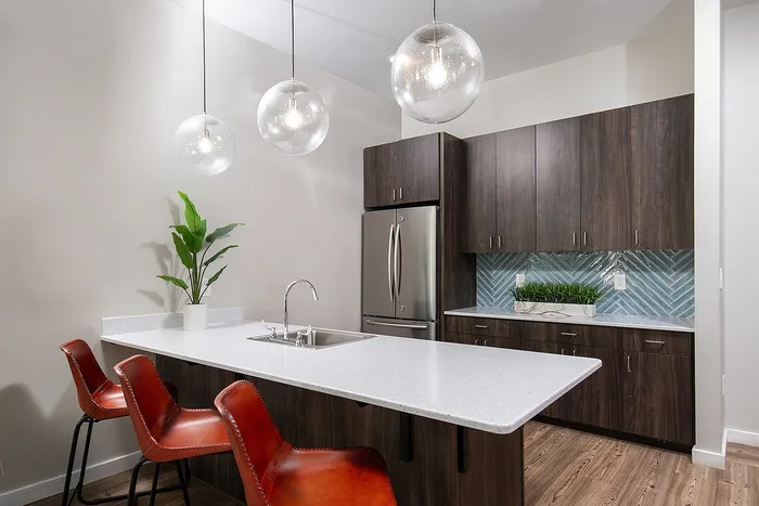 Modern kitchen featuring sleek dark wood cabinets, elegant pendant lighting, and a stylish breakfast bar with red chairs.